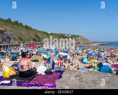 Folle che si godono la spiaggia di Sunny Sands a Folkestone, nel Kent, durante una vacanza solare, con ombrelloni, tende e turisti che riempiono il lungomare. Foto Stock