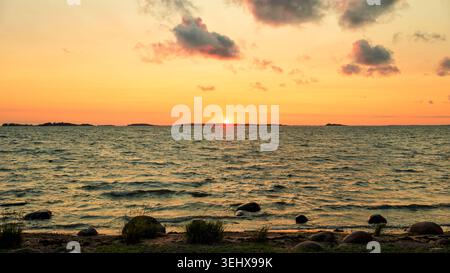 Hanko, Finlandia - 22.05.2026: Una vista panoramica di un tramonto dorato sulle calme acque del Mar Baltico, caratterizzato da una costa rocciosa e isole lontane in H. Foto Stock