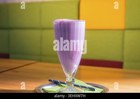 Frullato viola in un bicchiere alto su un tavolo con sfondo verde e arancione, Cafe Kuh, Deckenpfronn, Germania Foto Stock