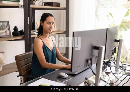 Donna concentrata che lavora su due monitor nell'ufficio domestico Foto Stock