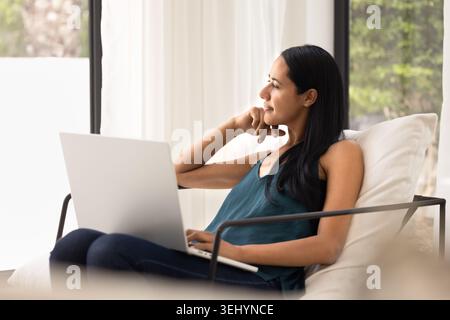 Donna pensiva che si rilassa con un notebook a casa Foto Stock