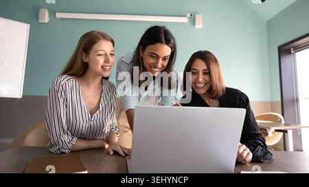 Le allegre collaboratrici di gruppo collaborano con un laptop al tavolo dell'ufficio Foto Stock
