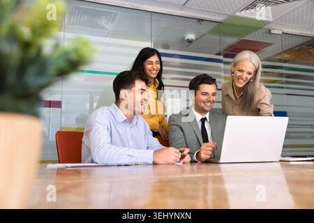Il team si è riunito intorno al notebook ridendo, guardando i contenuti, lavorando alla presentazione Foto Stock