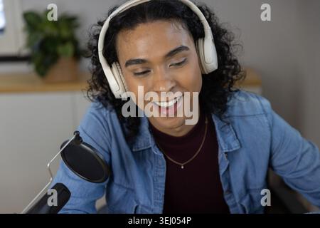 Persona non-binaria che indossa una maglietta in denim con microfono e cuffie bianche in casa Foto Stock