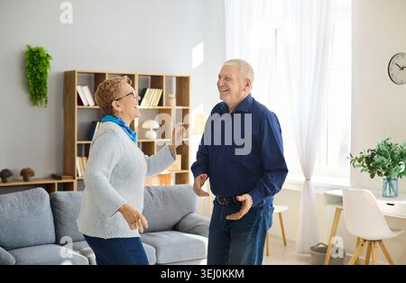 Felice coppia di anziani che ballano insieme a casa, godendo di benessere, amore e vitalità Foto Stock
