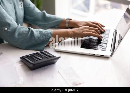 Donna che scrive su un notebook alla scrivania con documenti e calcolatrice Foto Stock