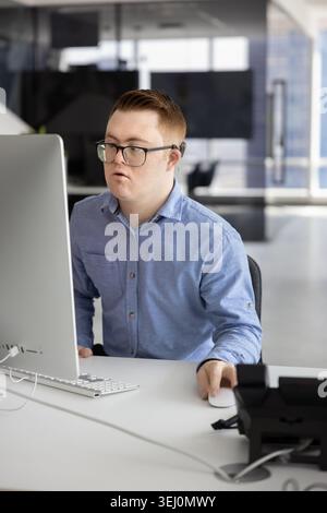 Giovane con sindrome di Down che lavora al computer in ufficio Foto Stock