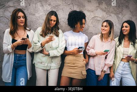 Raccolta di donne provenienti da diversi background che utilizzano smartphone mentre si trovano insieme all'esterno. Foto Stock