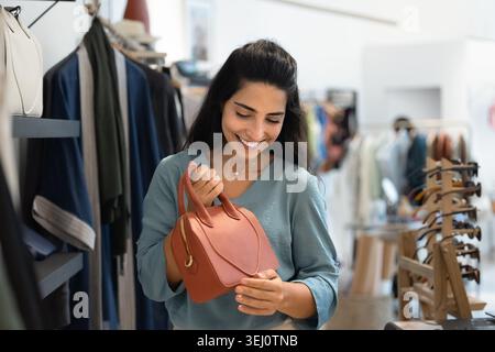 Giovane donna che esamina la borsa in pelle rossa nel negozio di moda Foto Stock