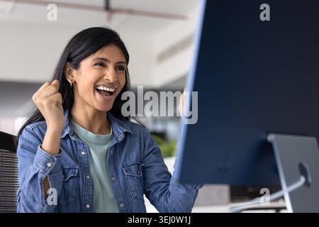 Una donna indiana felice celebra il successo professionale sul posto di lavoro Foto Stock