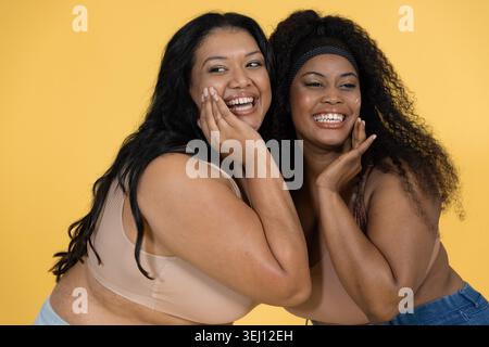 Diverse amiche di medie dimensioni che si presentano sorridenti in uno sfondo giallo denim con bralette color abbronzatura Foto Stock