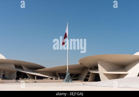 Doha, Qatar - 14 febbraio 2026: Un'ampia vista panoramica della bandiera nazionale del Qatar che sventola sopra il museo ispirato alle rose del deserto in Qatar. Foto Stock