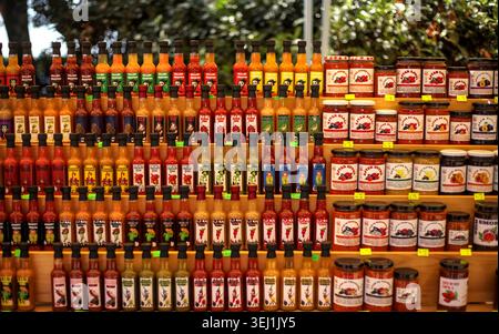 Ripiani in legno pieni di file di bottiglie di vetro contenenti salse calde fatte in casa e vasetti di marmellata dolce in un mercato locale di Opatija. Foto Stock