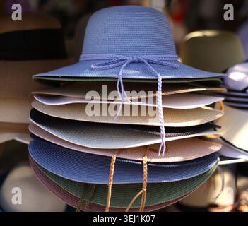 Un'ordinata pila verticale di colorati cappelli da donna in paglia a tesa larga con un prominente cappello in tessuto blu sulla parte superiore, mostrato in uno scatto ravvicinato. Foto Stock