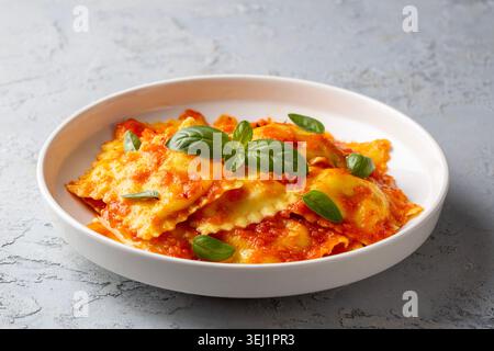Ravioli italiani fatti in casa con salsa di pomodoro e foglie di basilico fresco su un piatto bianco Foto Stock