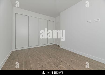 Una spaziosa camera da letto vuota con armadi a muro dal design lineare, lunghe maniglie cromate e che riflettono la luce naturale che scorre attraverso Foto Stock