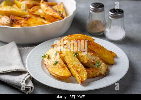 Spicchi di patate al forno con erbe e prezzemolo serviti in un recipiente di ceramica bianco Foto Stock