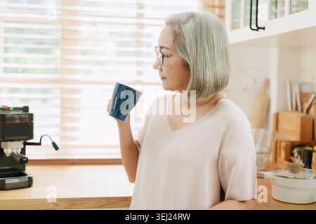 Donna asiatica anziana in piedi con la mano che tiene la tazza di caffè, il signore beve tè o caffè al mattino. Foto Stock
