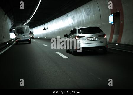 Un punto di vista di un veicolo in movimento all'interno di un tunnel sotterraneo di cemento curvo, che mostra un'auto argentata e un furgone bianco che precede Foto Stock