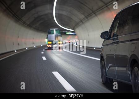 Un punto di vista ad angolo basso ripreso da un veicolo in movimento all'interno di un moderno tunnel sotterraneo in cemento, che mostra un furgone grigio e un veicolo sfocato Foto Stock