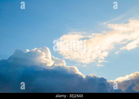 Le morbide e soffici nuvole fluttuano dolcemente contro un cielo blu vivace, creando un'atmosfera tranquilla. La luce del sole illumina le nuvole, esaltando la tua Foto Stock
