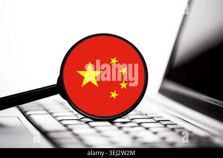 Concetto tecnologico cinese con lente di ingrandimento sulla tastiera del computer portatile. Economia digitale e concetto di cibersicurezza con bandiera cinese. Foto Stock