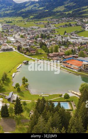 Villaggio alpino sul lago con prati verdi e colline, montagne sullo sfondo, vista aerea, Kirchberg, Austria Foto Stock