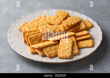 Pila di cracker croccanti dorati salati su un piatto bianco in ceramica Foto Stock