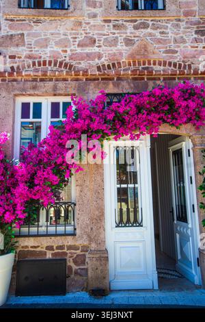 Ayvalik - Turkey, 17 maggio 2026, ingresso alla storica casa in pietra decorata con la vibrante Bougainvillea rosa sull'isola di Cunda Foto Stock