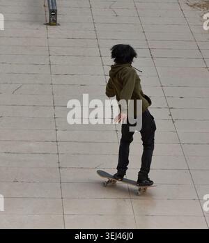 Parigi, Francia - 8 maggio 2026: Un giovane con una felpa verde cavalca uno skateboard su un marciapiede liscio in uno skate Park urbano, mostrando le sue abilità in un pub Foto Stock