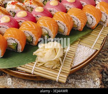 Cibo, coloratissimi sushi rotoli si trovano ordinati su un tappetino in bambù, con vari ingredienti. I rotoli rosa, arancione e rosso luminosi sono disposti in un ambiente accattivante Foto Stock