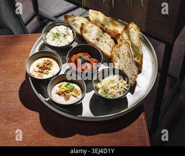 Cibo, Una collezione di cinque piccole ciotole riempite di vari salti viene presentata accanto a fette di pane fresco su un tavolo di legno. Questo arrangiamento appetitoso Foto Stock