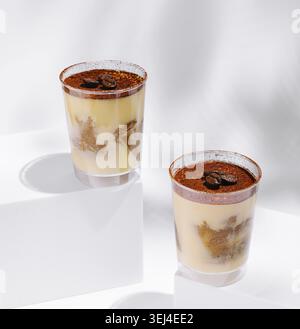 Cibo, due tazze trasparenti mostrano un dessert cremoso con strati di crema pasticcera e torta, ricoperto di cacao in polvere e chicchi di caffè. Luci luminose Foto Stock