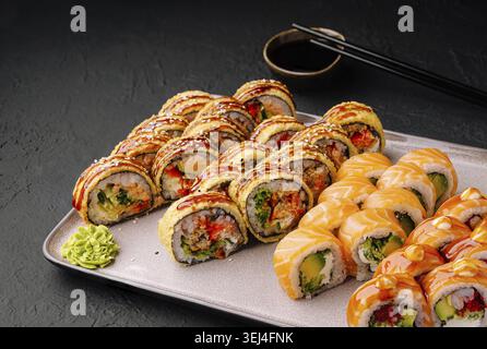 Cibo, coloratissimi sushi roll sono disposti ordinatamente su un piatto rettangolare. Vari ingredienti riempiono i panini, con salsa e wasabi a lato. Foto Stock