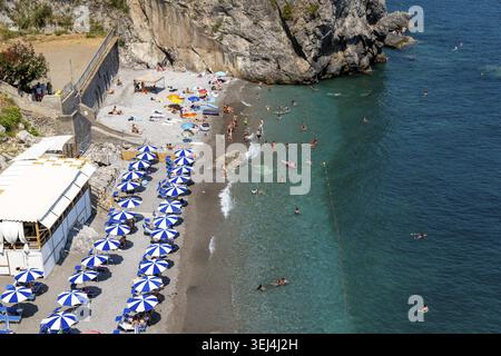 Amalfikueste - Kampanien - Italien - 07-04-2025: Spiaggia affollata con ombrelloni e bagnanti vicino a scogliere rocciose, acque turchesi e pendii costieri in Una Foto Stock