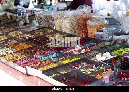 Uno stand del mercato espone un'ampia varietà di frutta secca, frutta secca e caramelle colorate in scomparti e sacchetti di plastica Foto Stock