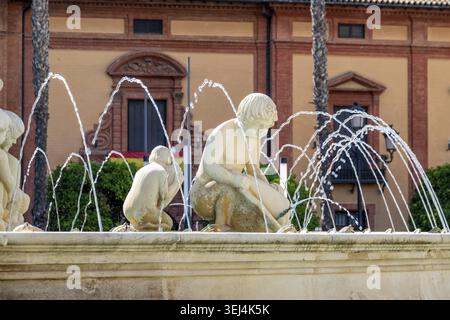 Siviglia, Siviglia - Spagna? 04-19-2024: Fontana in pietra AA con sculture per bambini, spruzzi d'acqua a forma di arco, illuminata dalla luce del sole Foto Stock