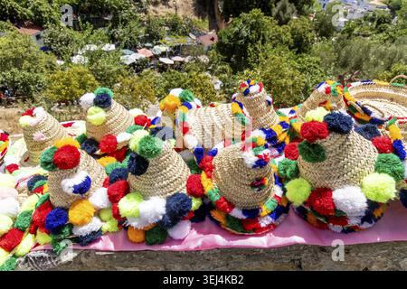 Cappelli di paglia con pomponi colorati in rosso, blu, verde, giallo e bianco su un panno rosa, circondati dal verde. Artigianato tradizionale marocchino Foto Stock