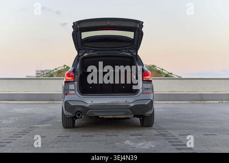 Un SUV moderno è parcheggiato sul tetto al tramonto, mostrando il suo bagagliaio aperto. La spaziosa area deposito è vuota e l'orizzonte è illuminato da serate soffici Foto Stock