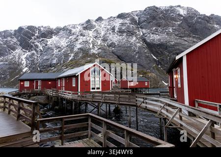 Una vista panoramica invernale delle storiche cabine rosse dei pescatori di rorbu collegate da passerelle in legno sopraelevate e piattaforme a palafitte sull'acqua, il Nusfjord Foto Stock