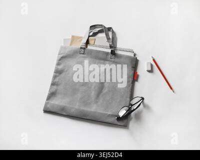 Borsa di tela grigia vuota, occhiali, matita e gomma su sfondo di carta Foto Stock