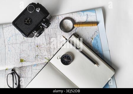 Fare un piano di viaggio. Mappa, blocco note vuoto, fotocamera, lente di ingrandimento, bussola, matita e occhiali. Posizione piatta Foto Stock