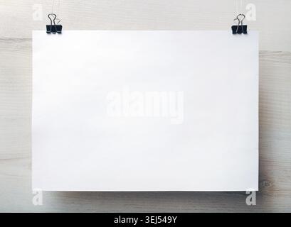 Poster bianco bianco appeso su sfondo in legno chiaro. Modello vuoto per posizionare il progetto. Vista frontale Foto Stock
