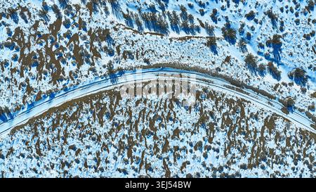 Strada coperta di neve aerea e vegetazione del deserto in inverno dall'alto verso il basso Foto Stock