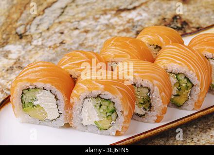 Cibo, sushi al salmone fresco si trovano ordinatamente su un piatto bianco. Sono piene di cetriolo e formaggio spalmabile, che mostrano colori vivaci in un caldo restau Foto Stock