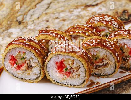 Cibo, sushi roll freschi con vari ripieni e condimenti disposti ordinatamente su un piatto bianco. I panini sono guarniti con una salsa saporita e. Foto Stock