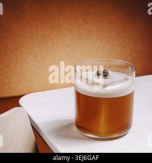 Cibo, Un cocktail di caffè freddo si trova su un tavolo elegante con uno sfondo caldo. La bevanda è caratterizzata da schiuma cremosa e chicchi di caffè, invitando a un rif Foto Stock