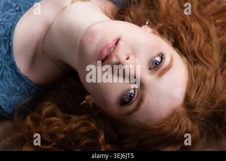 Giovane donna con accattivanti occhi blu e capelli rossi fluenti sentendosi connessa Foto Stock