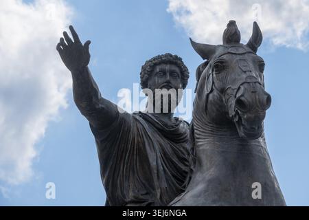 Impressionante statua equestre in bronzo scuro di Marc Aurel con una mano sollevata, testa di cavallo e brilla prominente contro il cielo blu con nuvole Foto Stock