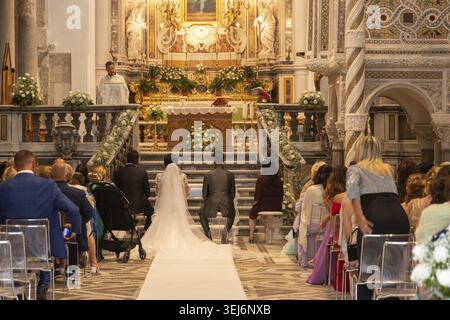 Sessa Aurunca - Campania - Italia - 08-29-2025: All'interno della Cattedrale di Sessa un sacerdote conduce una cerimonia nuziale mentre la coppia si inginocchia davanti all'alta ornata Foto Stock